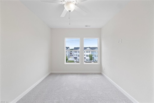 empty room featuring visible vents, light carpet, baseboards, and ceiling fan