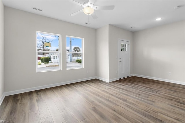 spare room featuring ceiling fan, visible vents, baseboards, and wood finished floors