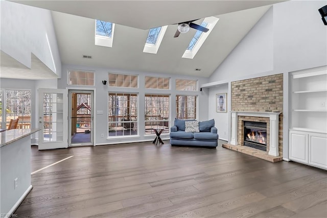 unfurnished living room with visible vents, high vaulted ceiling, dark wood finished floors, a skylight, and a fireplace