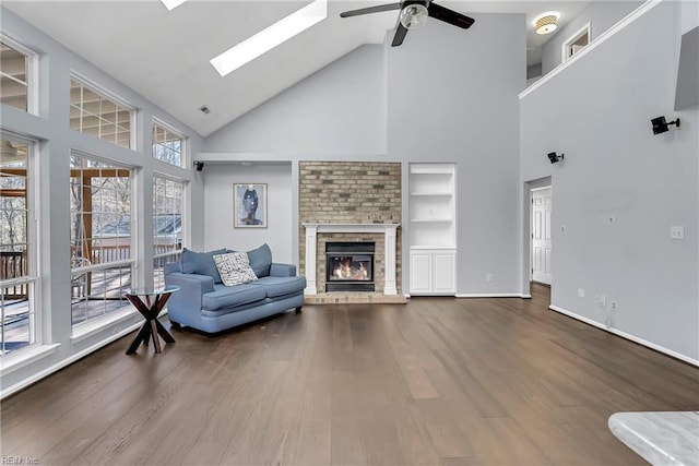 living area with a skylight, wood finished floors, a brick fireplace, and ceiling fan