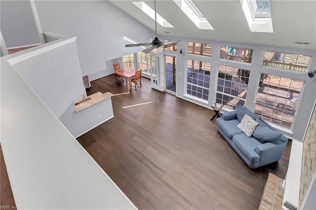 living room featuring wood finished floors, visible vents, high vaulted ceiling, a skylight, and ceiling fan