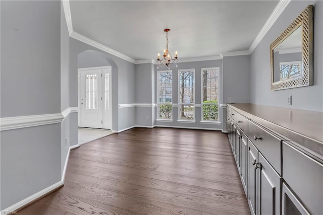 unfurnished dining area featuring dark wood-type flooring, baseboards, crown molding, a chandelier, and arched walkways