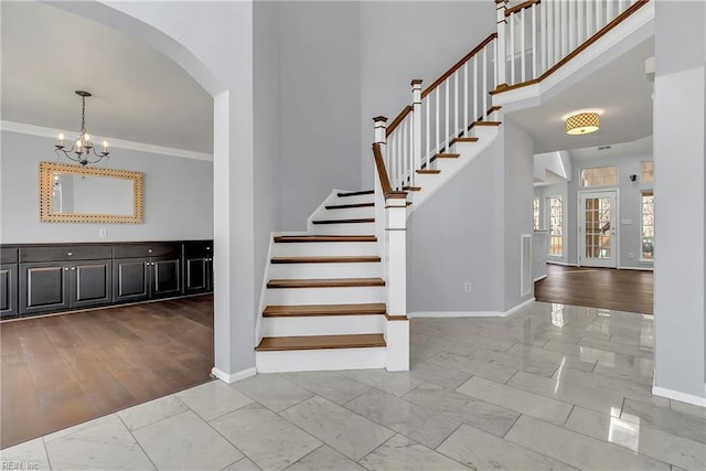 stairway featuring baseboards, an inviting chandelier, arched walkways, ornamental molding, and marble finish floor