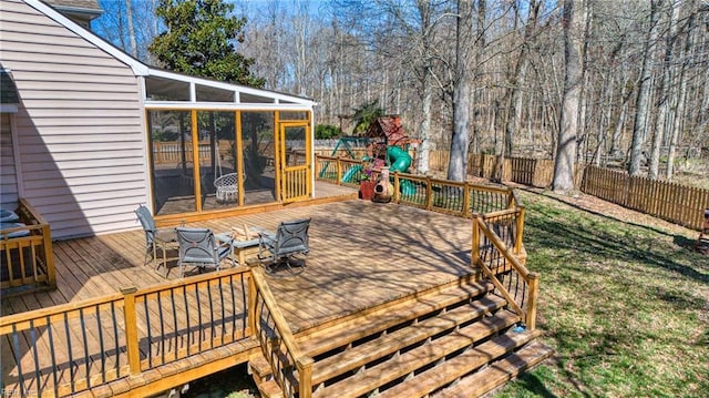 deck featuring a playground, fence, an outdoor fire pit, and a sunroom