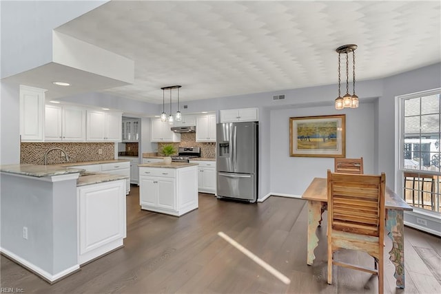 kitchen featuring under cabinet range hood, dark wood finished floors, hanging light fixtures, white cabinets, and stainless steel appliances