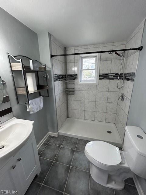 bathroom featuring vanity, baseboards, tiled shower, tile patterned floors, and toilet