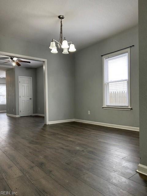 spare room featuring ceiling fan with notable chandelier, dark wood-style floors, and baseboards