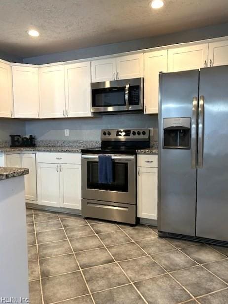 kitchen with dark stone countertops, dark tile patterned flooring, recessed lighting, stainless steel appliances, and white cabinets