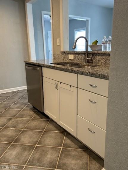 kitchen featuring dark tile patterned flooring, dark stone counters, stainless steel dishwasher, white cabinets, and a sink