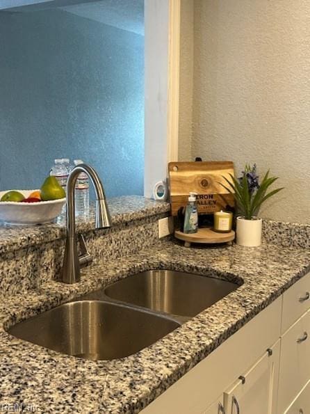 interior details featuring stone counters, white cabinetry, a textured wall, and a sink