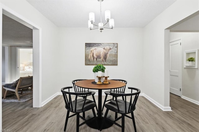 dining room with a notable chandelier, light wood-style flooring, a textured ceiling, and baseboards