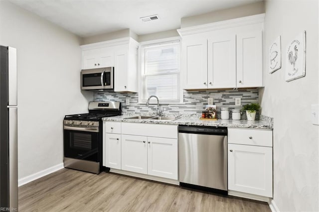 kitchen featuring visible vents, a sink, decorative backsplash, appliances with stainless steel finishes, and light wood-type flooring