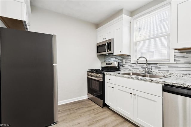 kitchen with light wood-style flooring, a sink, stainless steel appliances, white cabinetry, and backsplash