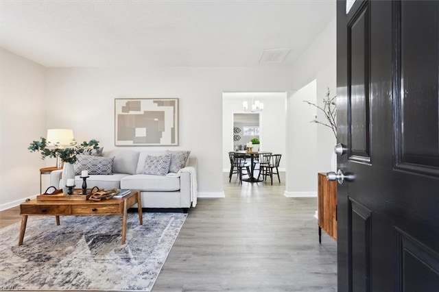 living area featuring visible vents, a notable chandelier, baseboards, and light wood-type flooring