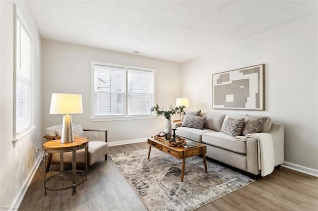 living room with visible vents, baseboards, a textured ceiling, and wood finished floors