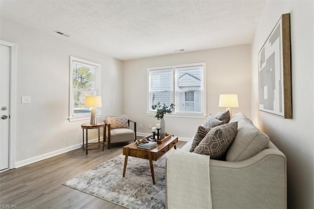 living area with visible vents, baseboards, a textured ceiling, and wood finished floors