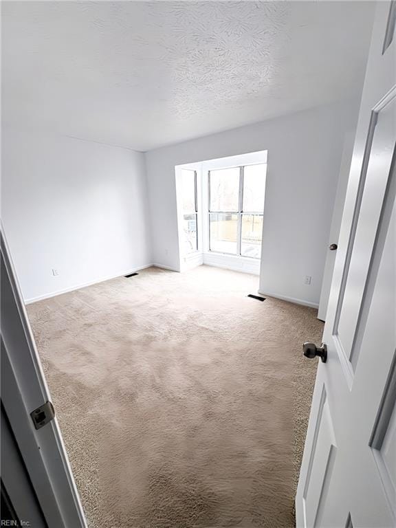 carpeted spare room featuring visible vents, a textured ceiling, and baseboards