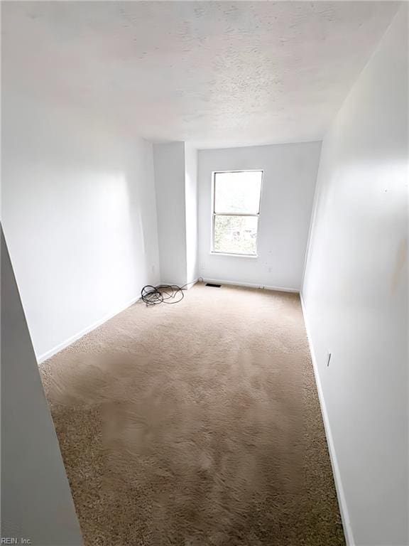 empty room featuring light carpet, visible vents, a textured ceiling, and baseboards