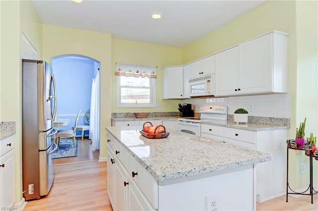 kitchen featuring tasteful backsplash, a center island, white cabinetry, white appliances, and arched walkways