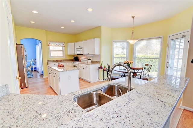 kitchen featuring white appliances, arched walkways, a sink, white cabinets, and light wood-type flooring