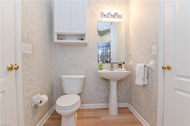 bathroom with baseboards, toilet, wood finished floors, and wallpapered walls