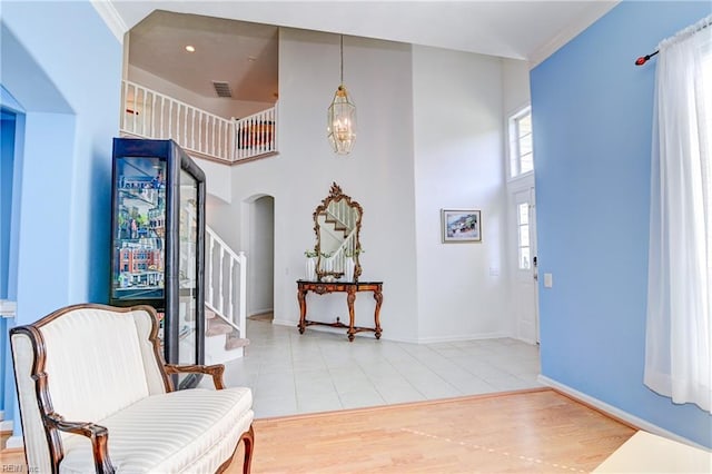 foyer entrance with an inviting chandelier, arched walkways, stairs, a towering ceiling, and light wood-type flooring