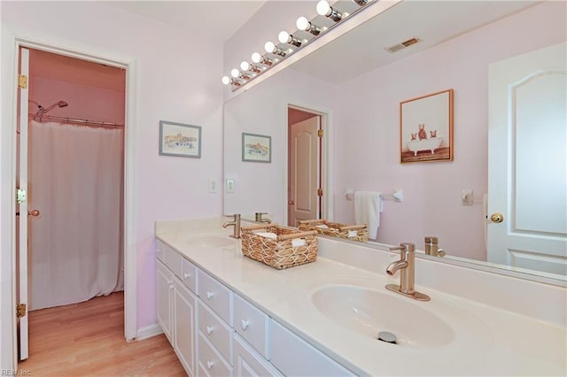 full bathroom featuring double vanity, wood finished floors, visible vents, and a sink