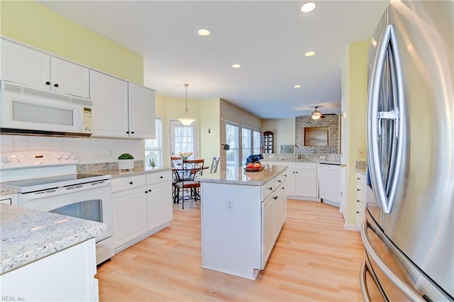 kitchen featuring backsplash, a center island, light wood-type flooring, white cabinets, and white appliances