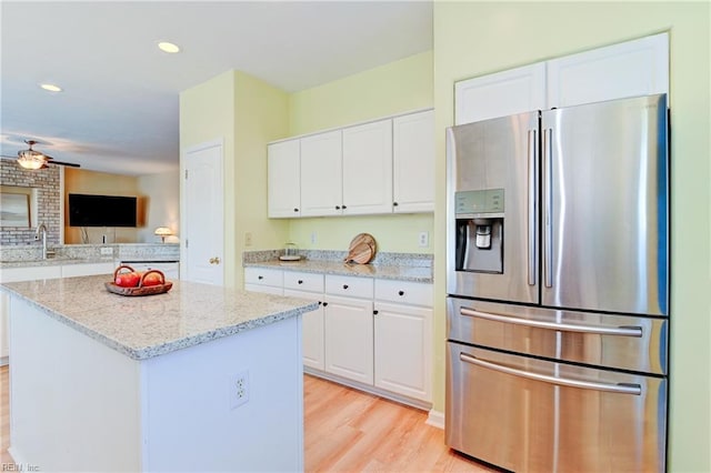 kitchen with stainless steel fridge, white cabinetry, and light stone countertops