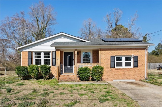 view of front of house with brick siding, roof mounted solar panels, a porch, and fence