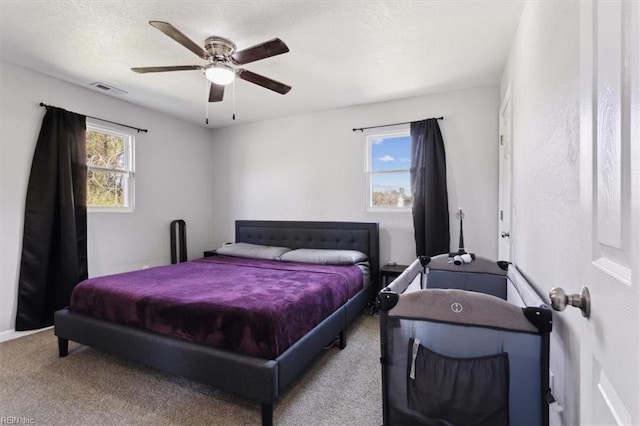 carpeted bedroom with visible vents, multiple windows, a textured ceiling, and ceiling fan