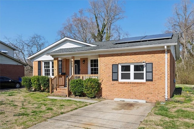 view of front of property with brick siding, a shingled roof, a porch, a front yard, and roof mounted solar panels