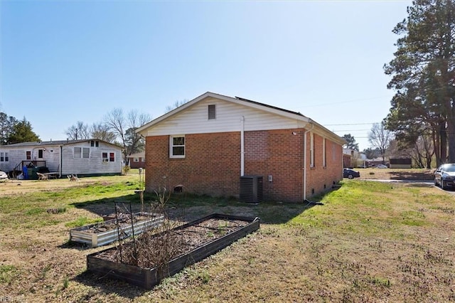 back of house featuring a vegetable garden, central AC, crawl space, a lawn, and brick siding