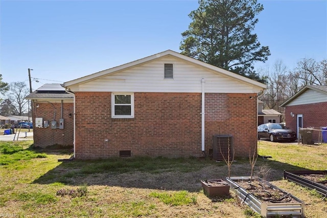 view of property exterior with a garden, a yard, crawl space, brick siding, and roof mounted solar panels