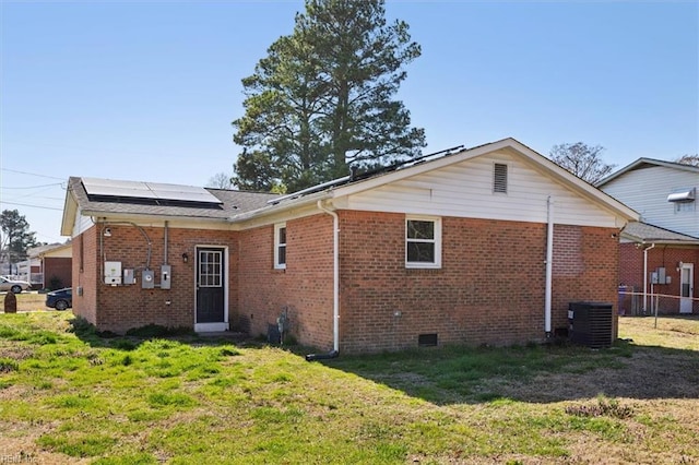 rear view of property with brick siding, central air condition unit, roof mounted solar panels, a yard, and crawl space