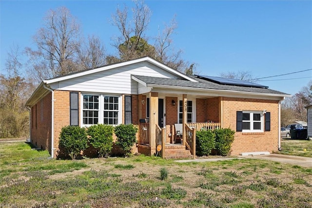 view of front of property featuring brick siding, covered porch, solar panels, and a front yard