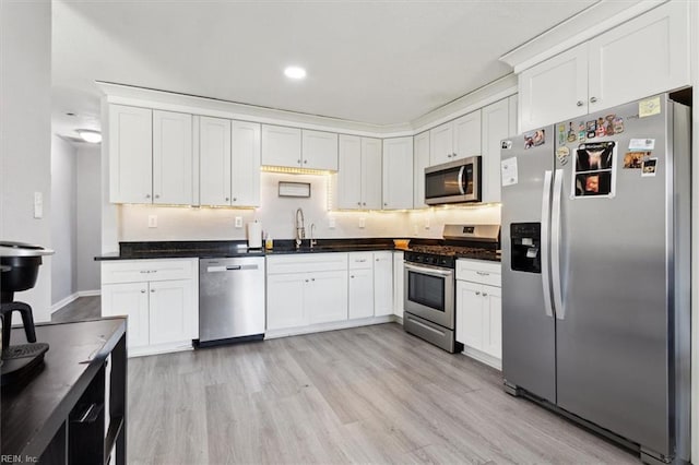 kitchen with a sink, stainless steel appliances, light wood-type flooring, and dark countertops