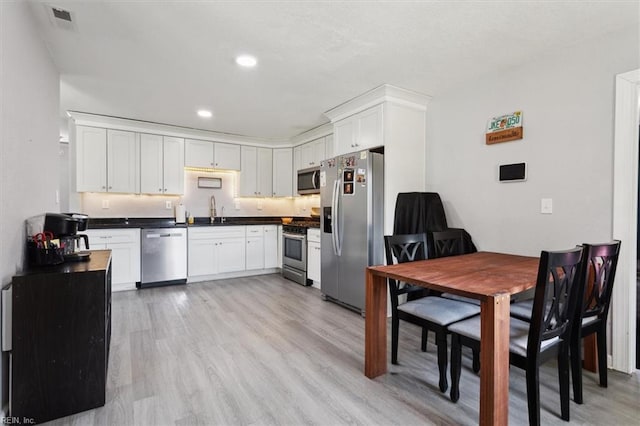 kitchen featuring visible vents, light wood finished floors, a sink, stainless steel appliances, and dark countertops