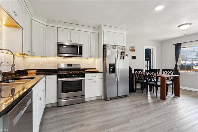 kitchen with baseboards, light wood-style flooring, a sink, stainless steel appliances, and white cabinets