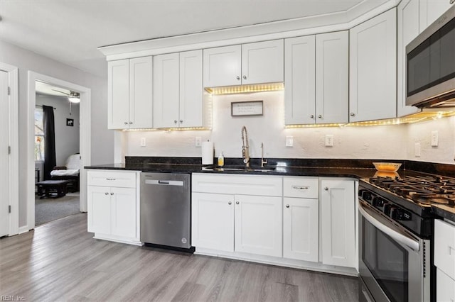 kitchen featuring light wood-style flooring, a sink, white cabinets, appliances with stainless steel finishes, and backsplash