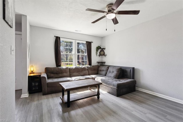 living room featuring a textured wall, a ceiling fan, baseboards, and wood finished floors