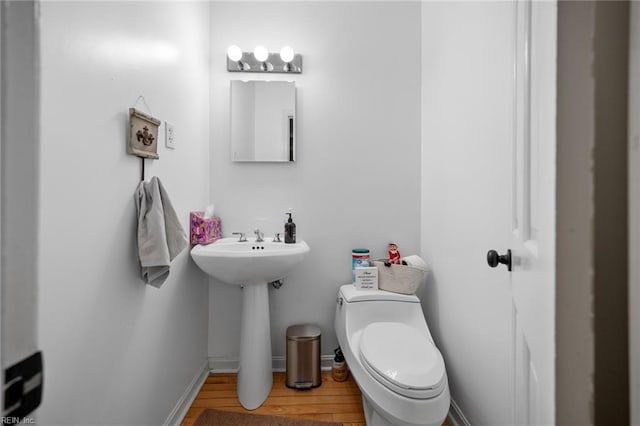 half bathroom with baseboards, toilet, and wood finished floors