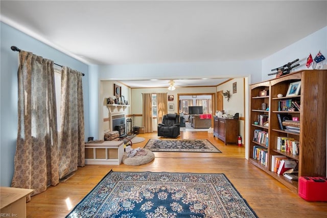 living room with a fireplace with raised hearth, a ceiling fan, and wood finished floors