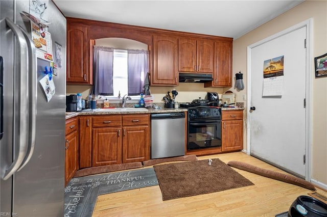 kitchen with a sink, brown cabinetry, under cabinet range hood, and stainless steel appliances