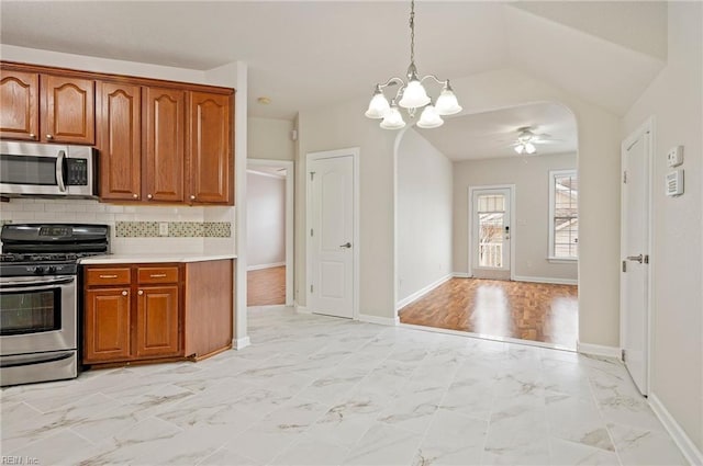 kitchen with light countertops, decorative backsplash, appliances with stainless steel finishes, brown cabinetry, and marble finish floor