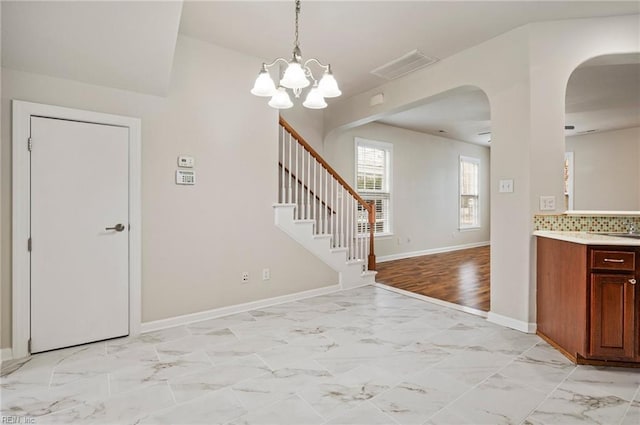 interior space with a notable chandelier, marble finish floor, arched walkways, baseboards, and stairs