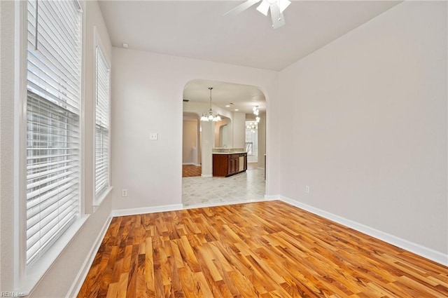 spare room featuring plenty of natural light, ceiling fan with notable chandelier, arched walkways, and light wood-type flooring