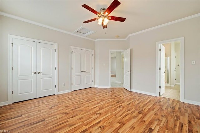 unfurnished bedroom with baseboards, attic access, multiple closets, crown molding, and light wood-type flooring