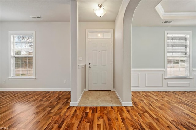 foyer with visible vents, wood finished floors, arched walkways, wainscoting, and a decorative wall