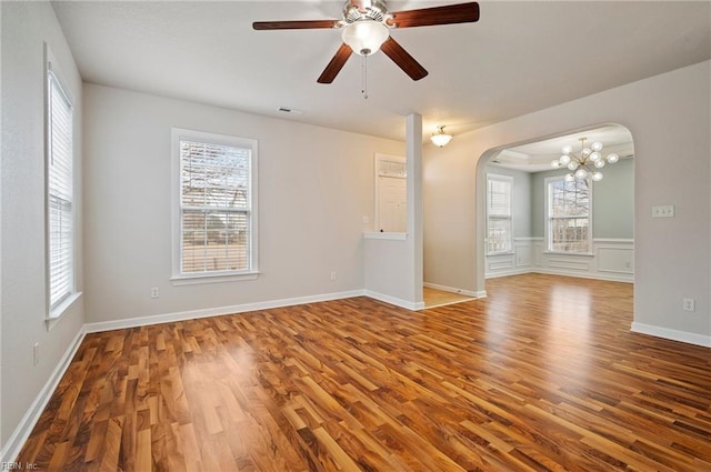 empty room featuring visible vents, baseboards, ceiling fan with notable chandelier, wood finished floors, and arched walkways